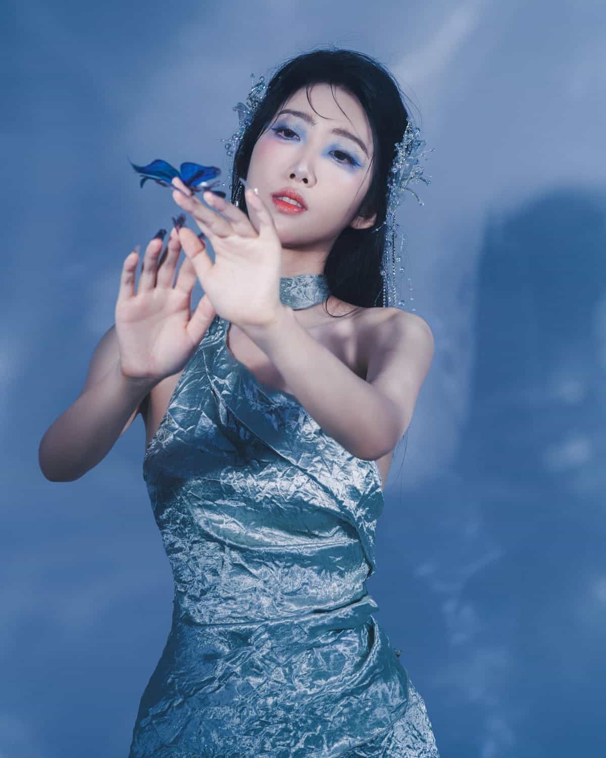 Portrait d’une femme dans une ambiance bleue, la main tendue vers un papillon.
